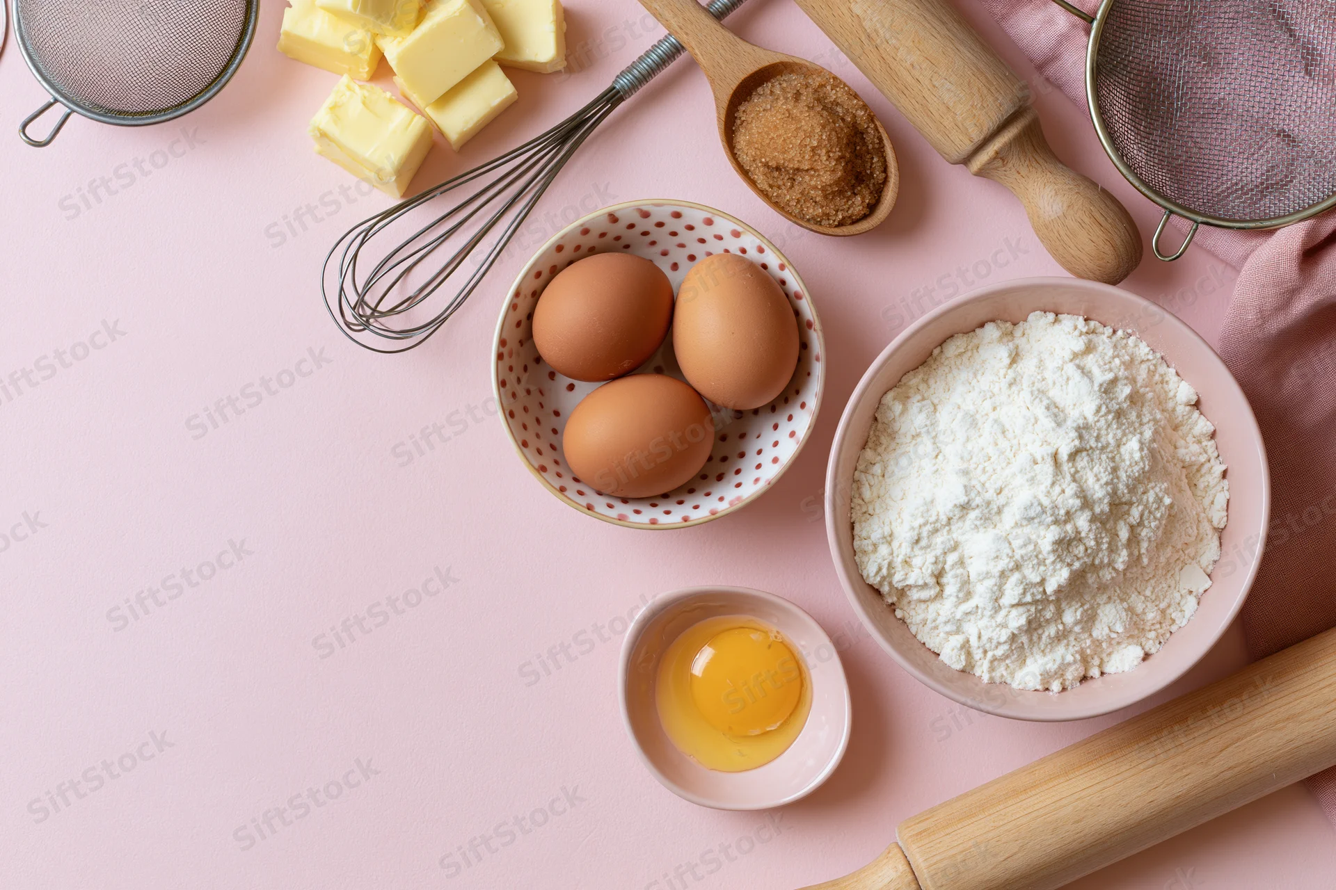 Baking ingredients arranged on a pink surface with utensils and copyspace