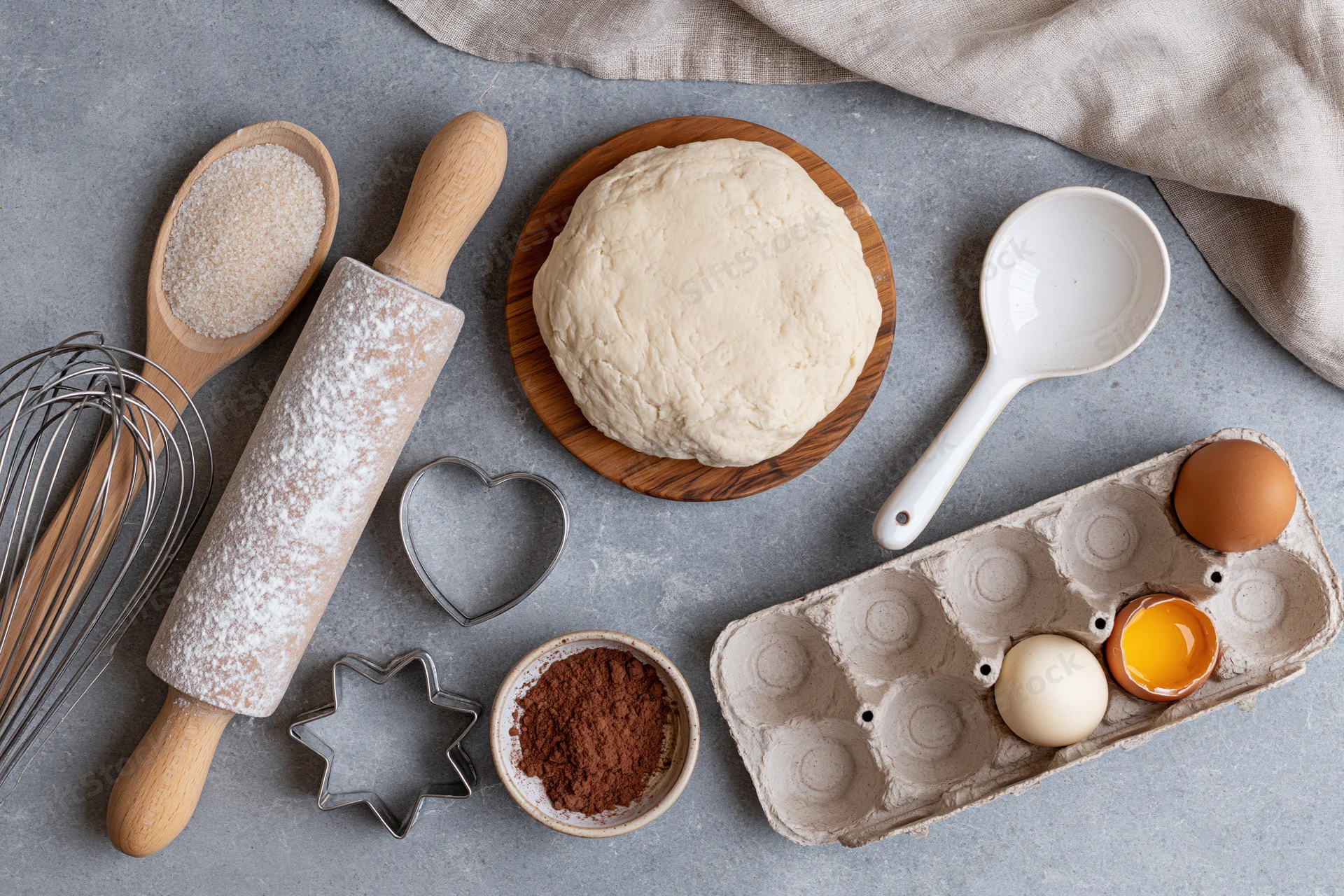 Dough ball on wooden board surrounded by baking ingredients and tools on gray countertop