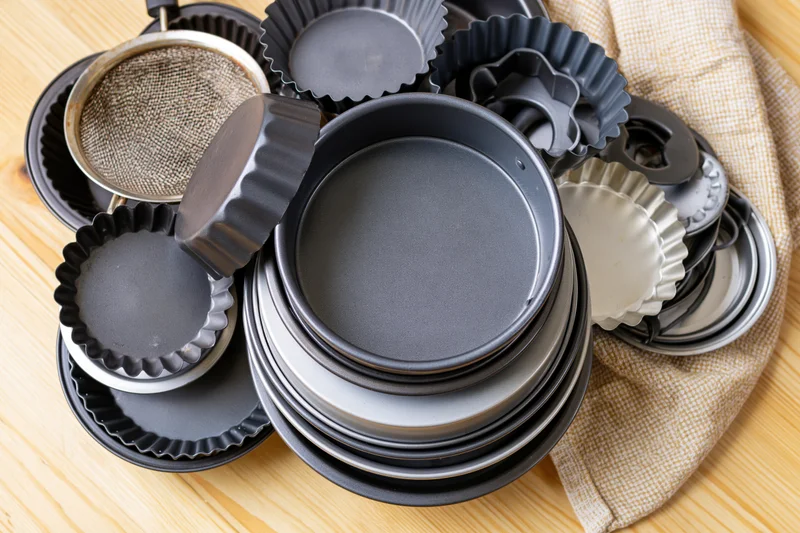 Various baking pans and molds stacked on a wooden surface with a cloth napkin