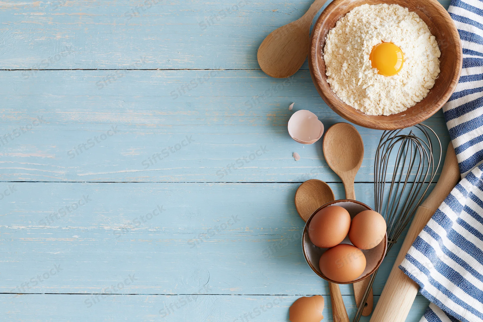 Baking ingredients arranged on a blue wooden tabletop with copyspace
