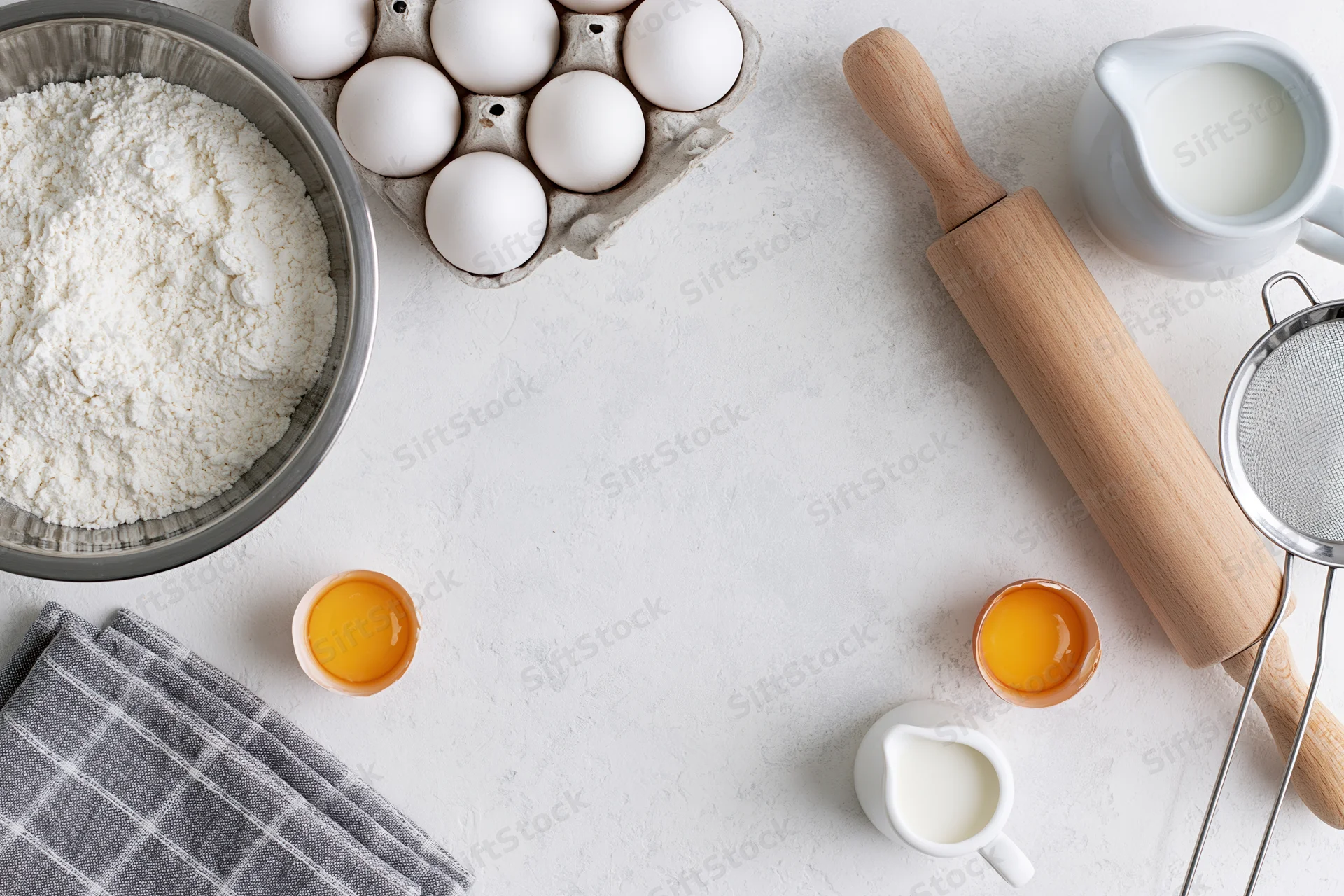 Baking ingredients arranged on a white countertop with rolling pin and sieve