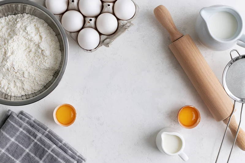 Baking ingredients arranged on a white countertop with rolling pin and sieve