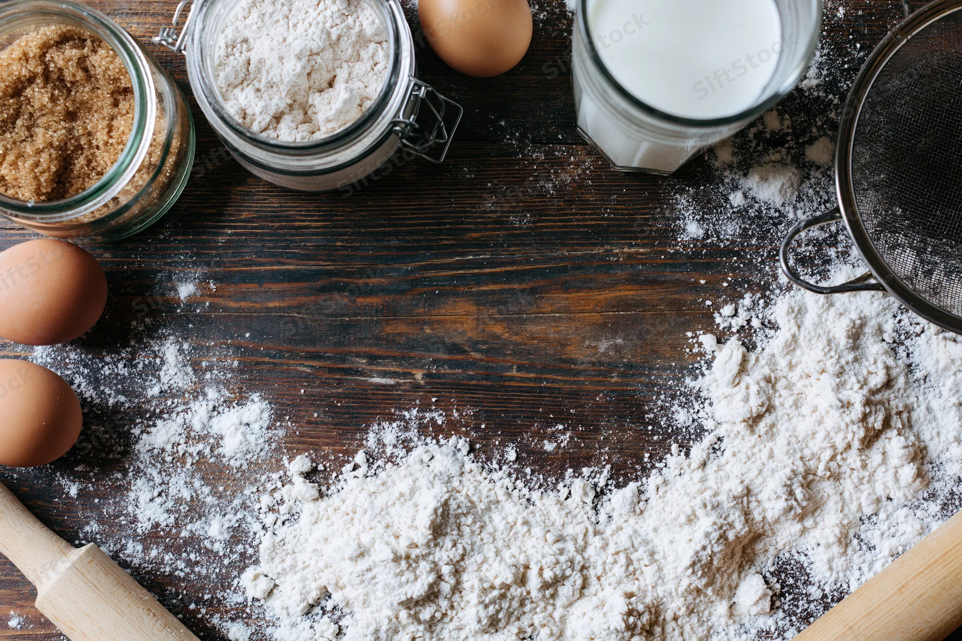 Flour and baking ingredients arranged on a dark wooden table with copyspace