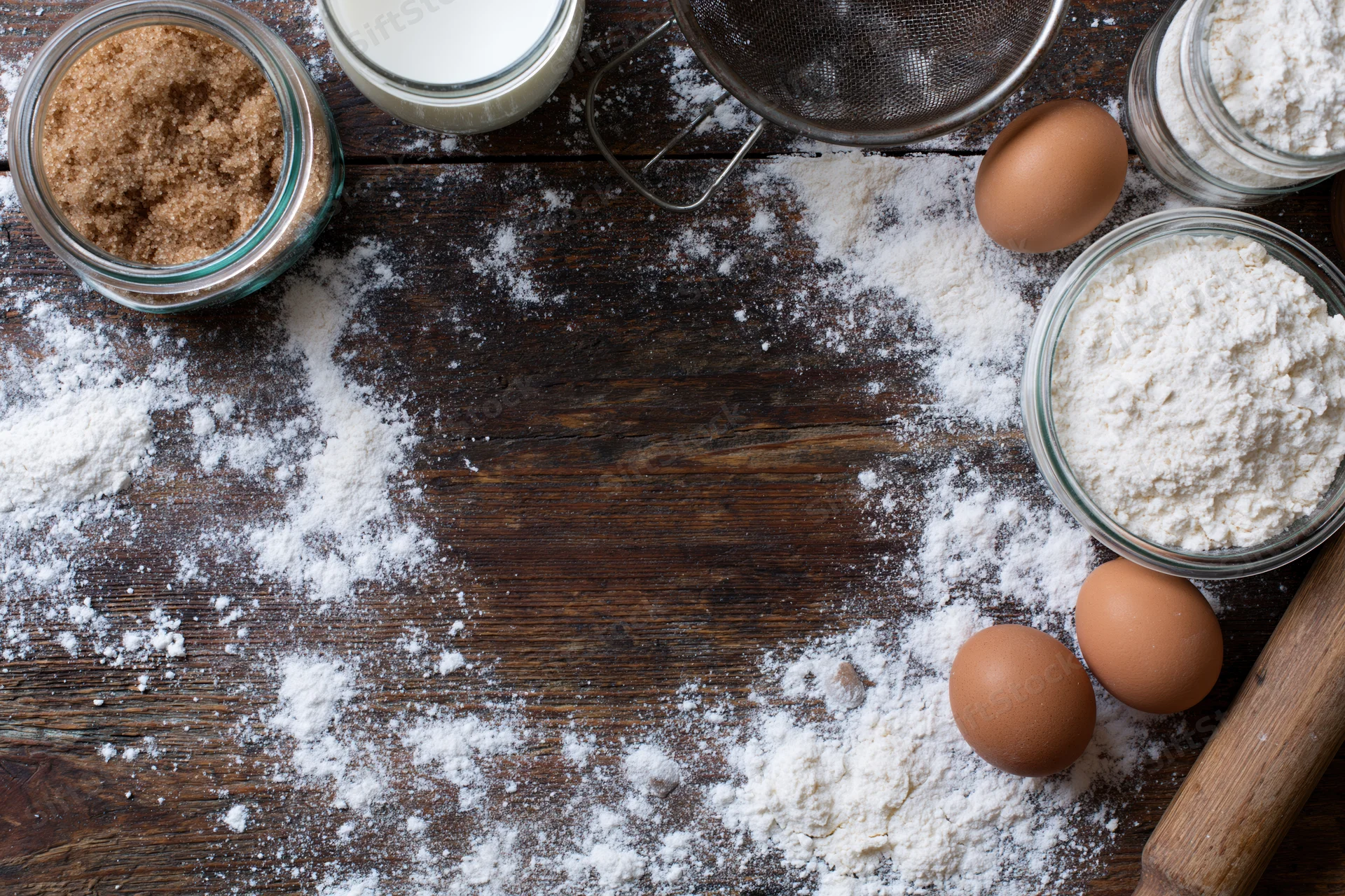 Baking ingredients arranged on a wooden table with flour dusted across the surface