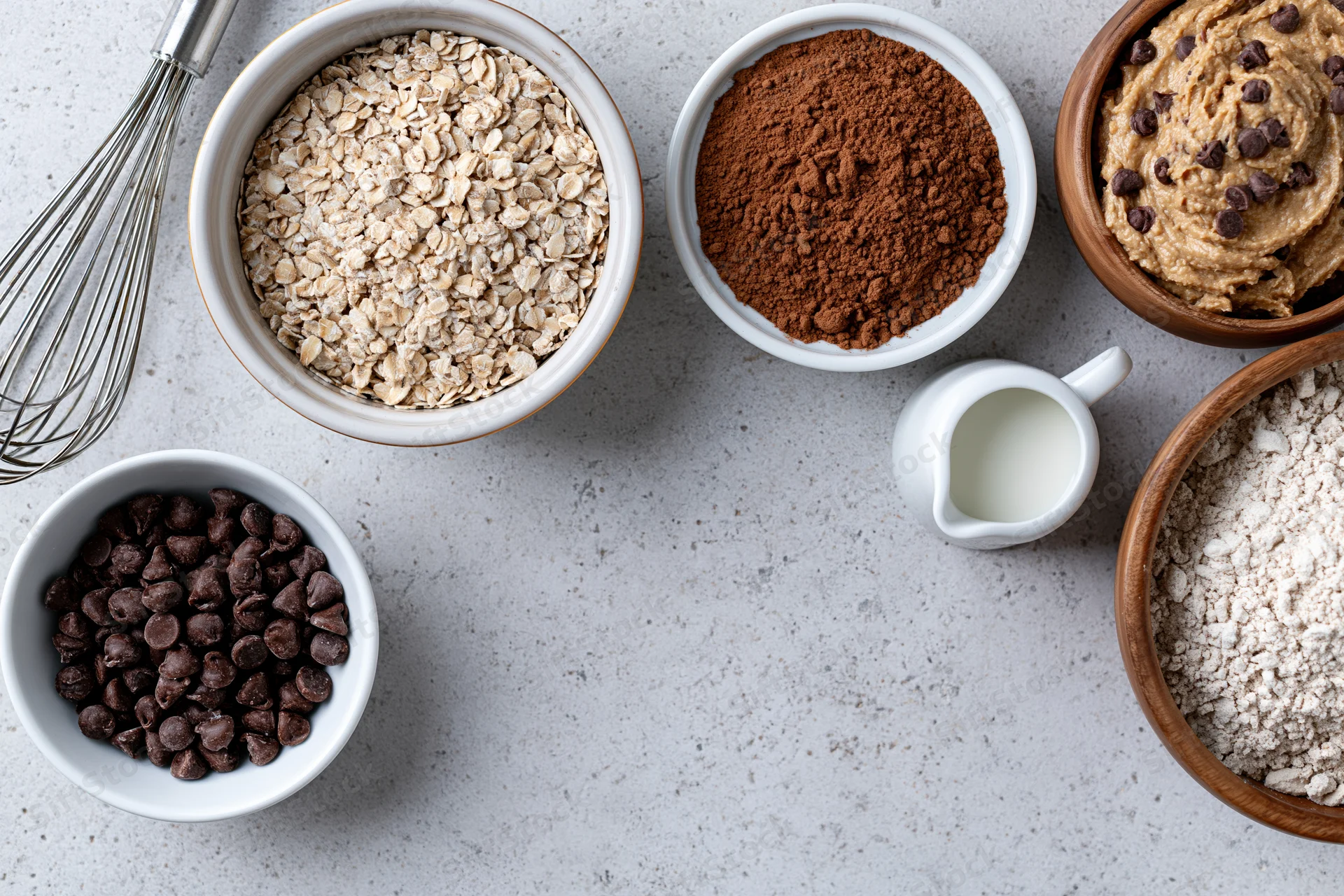 Various baking ingredients arranged in bowls on a countertop with a whisk and milk jug nearby