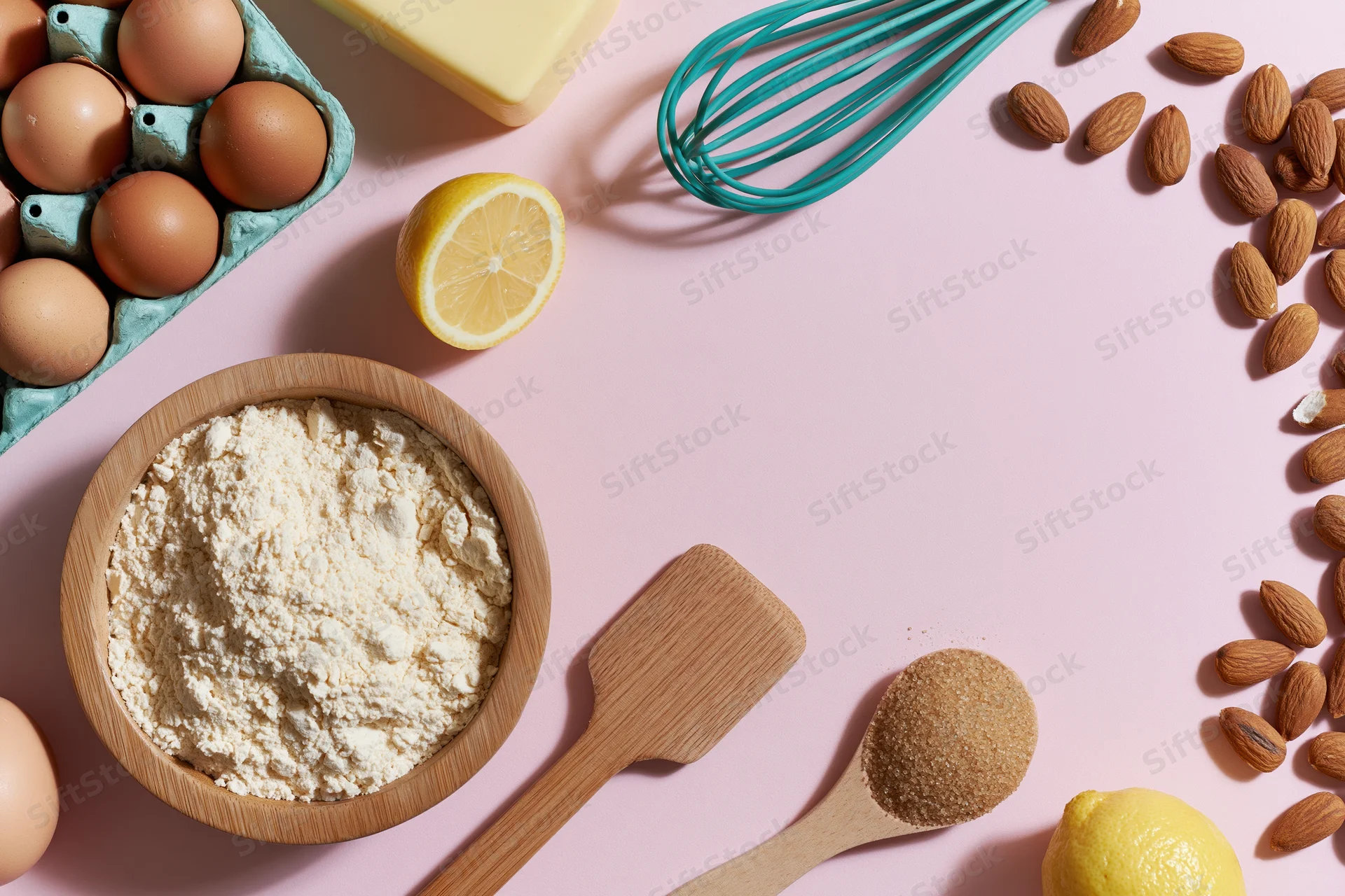 Baking ingredients arranged on pink surface with wooden utensils and copyspace