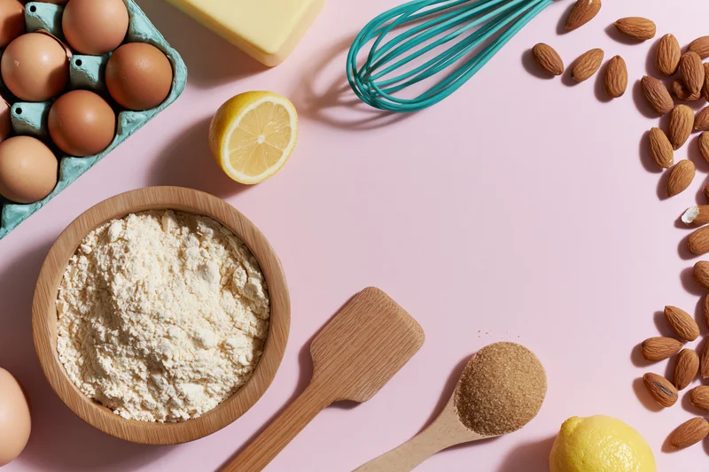 Baking ingredients arranged on pink surface with wooden utensils and copyspace