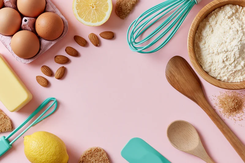 Baking ingredients and tools arranged on a pink surface in a flat lay composition
