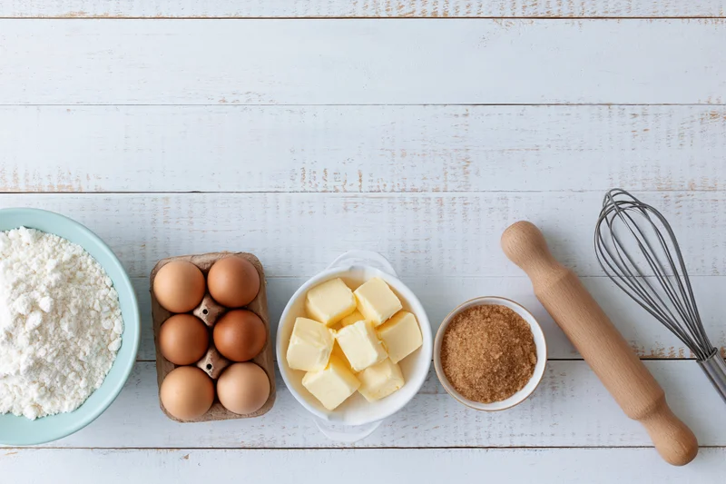 Baking ingredients arranged on a white wooden countertop in overhead flatlay view