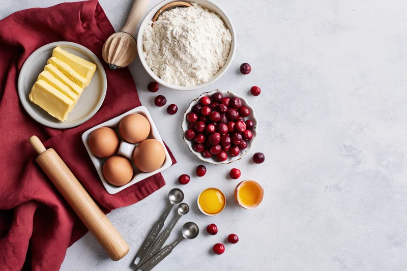 Baking ingredients including cranberries, flour, butter, eggs and a rolling pin arranged on a countertop with copyspace