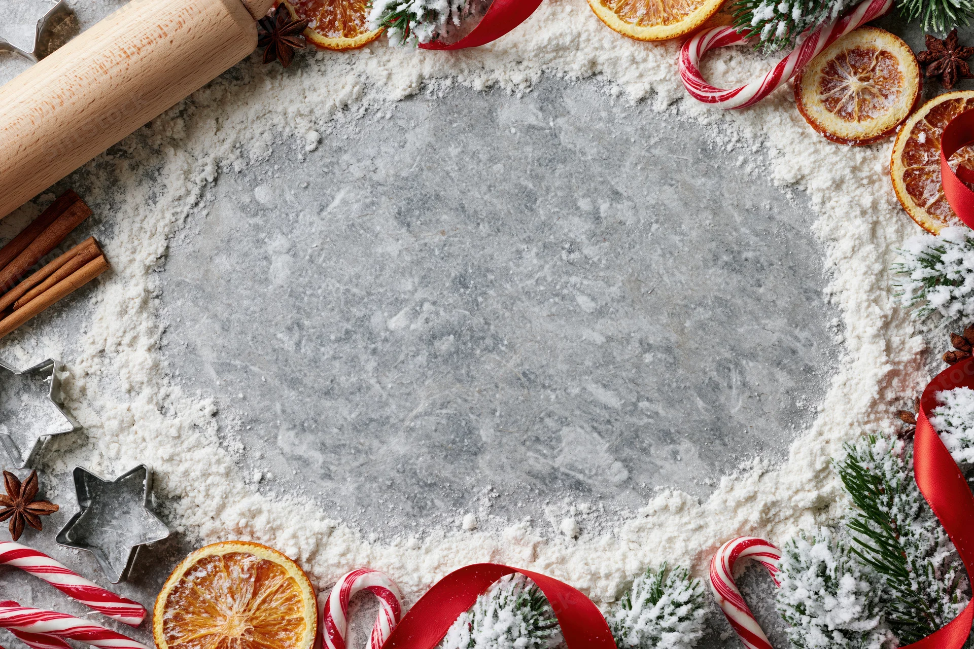 Festive holiday baking setup with flour, candy canes, dried oranges and pine on countertop