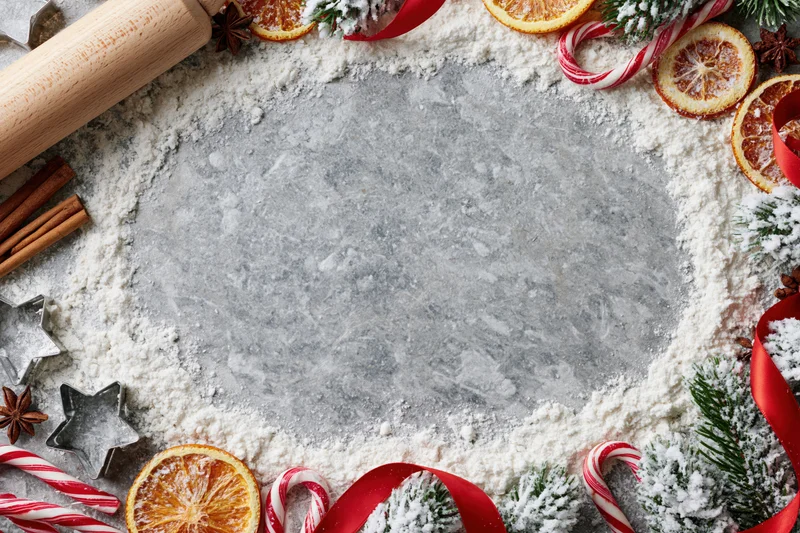 Festive holiday baking setup with flour, candy canes, dried oranges and pine on countertop