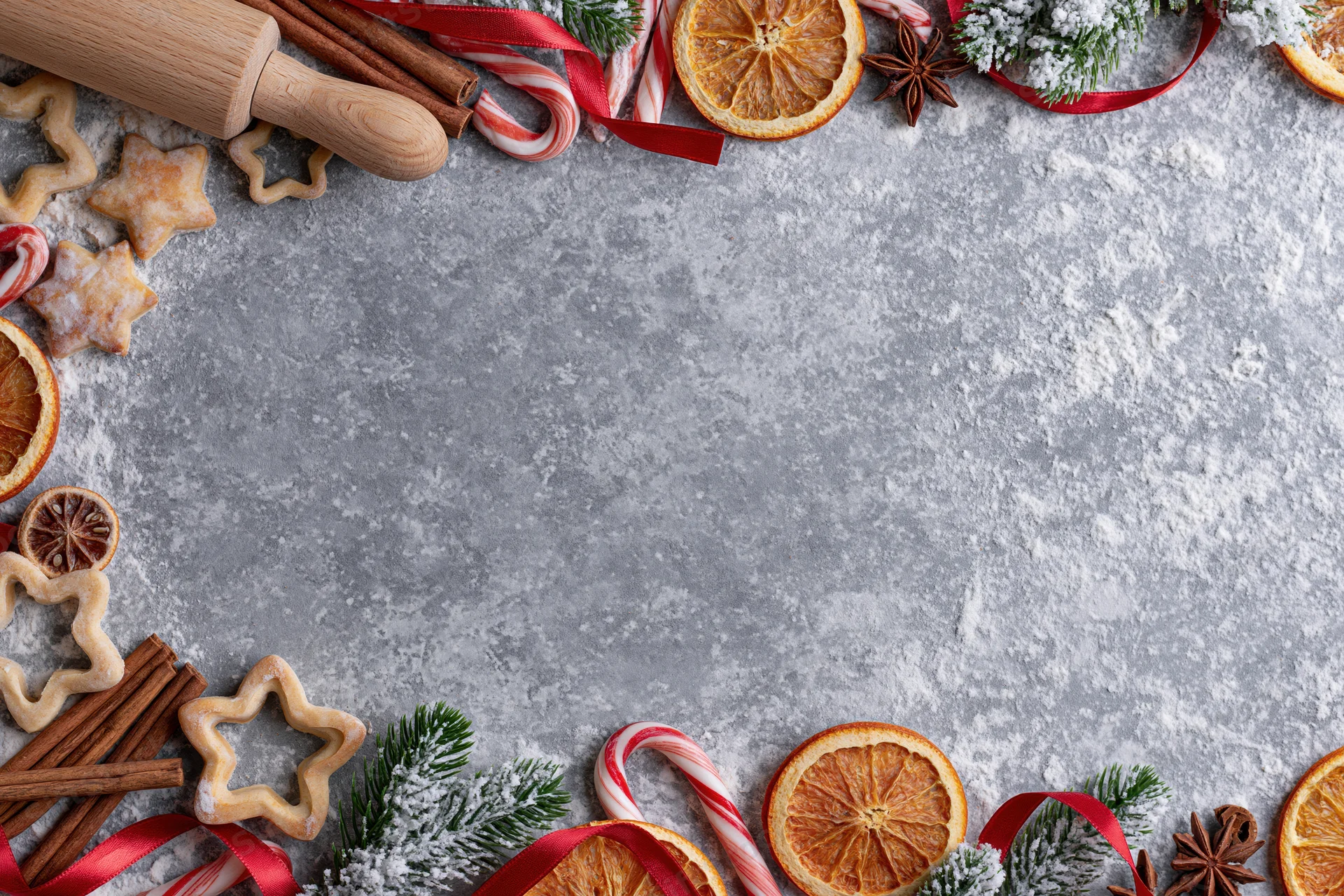 Christmas baking ingredients and decorations arranged along the edges of a gray countertop with copyspace in the center