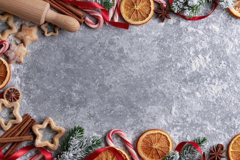 Christmas baking ingredients and decorations arranged along the edges of a gray countertop with copyspace in the center