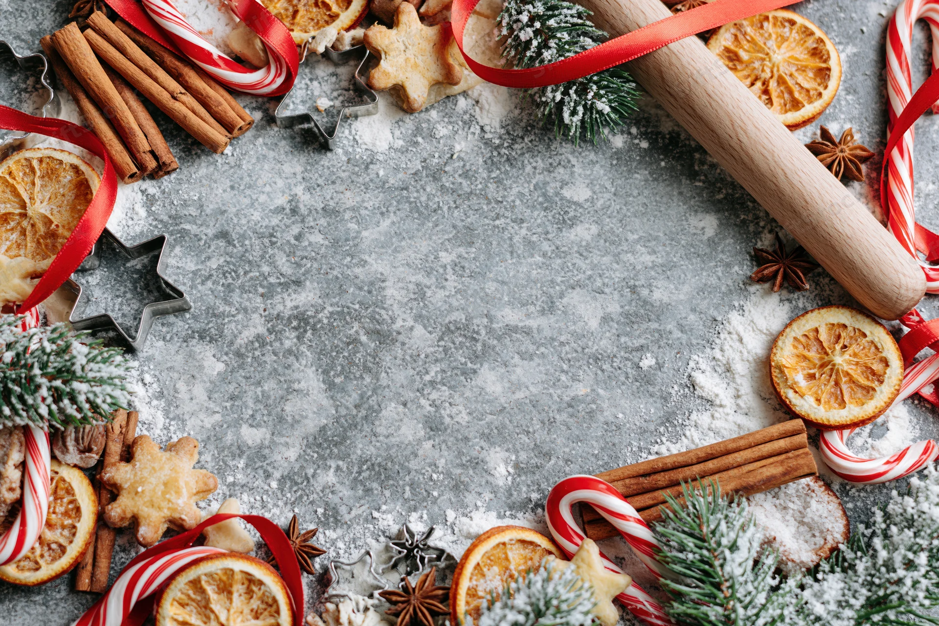 Christmas baking ingredients arranged in a festive border on a floured countertop with copyspace in center