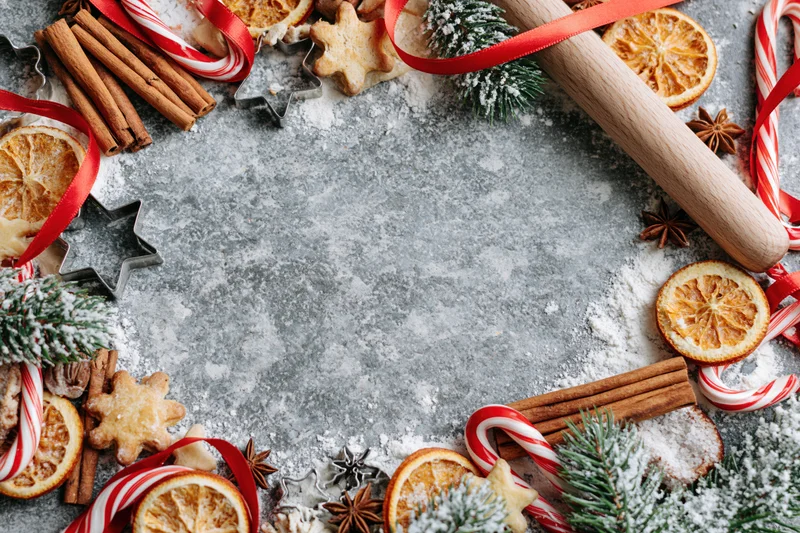 Christmas baking ingredients arranged in a festive border on a floured countertop with copyspace in center