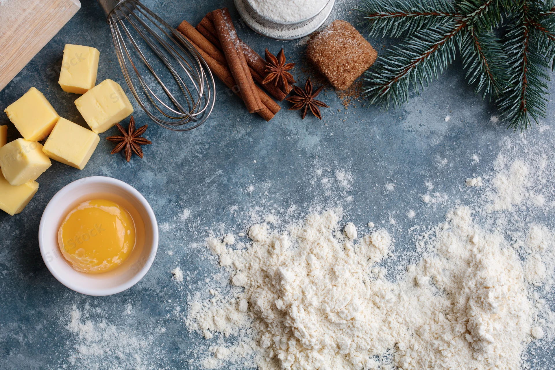 Baking ingredients arranged on a blue countertop with flour, butter, egg, cinnamon and star anise for holiday preparation