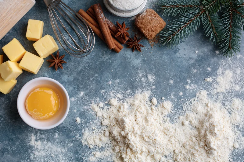 Baking ingredients arranged on a blue countertop with flour, butter, egg, cinnamon and star anise for holiday preparation
