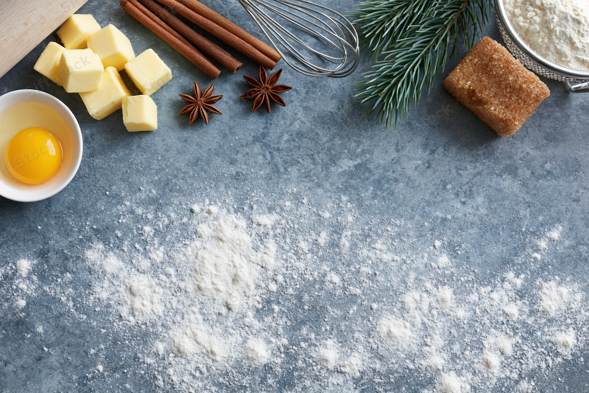Baking ingredients arranged on a floured countertop with pine sprigs and spices for holiday dessert preparation