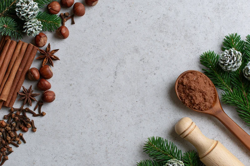 Cinnamon sticks, spices, pine branches and hazelnuts arranged on a light surface with a wooden spoon and grinder, festive holiday flat lay