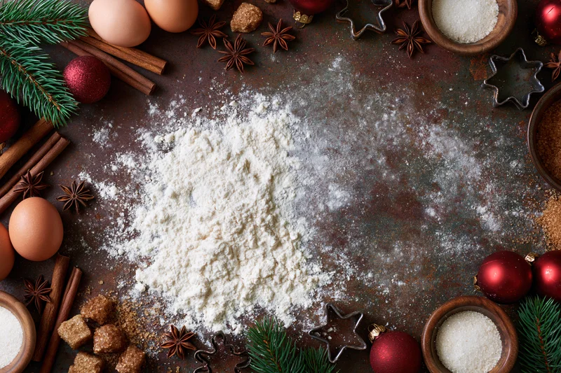 Flour and baking ingredients arranged around a rustic countertop with christmas decorations