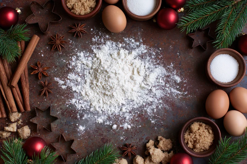 Flour and baking ingredients arranged with christmas decorations on a rustic surface