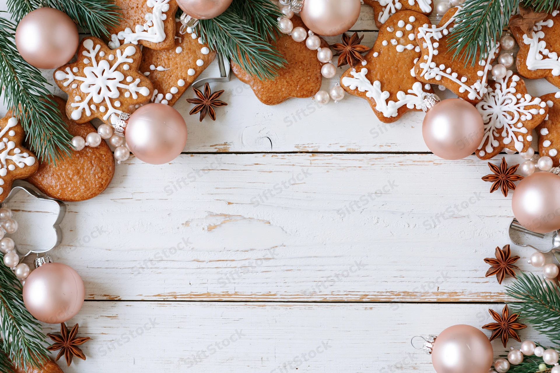 Gingerbread cookies and christmas ornaments arranged in a border on a white wooden surface with copyspace in the center