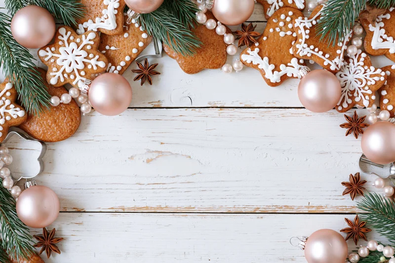 Gingerbread cookies and christmas ornaments arranged in a border on a white wooden surface with copyspace in the center