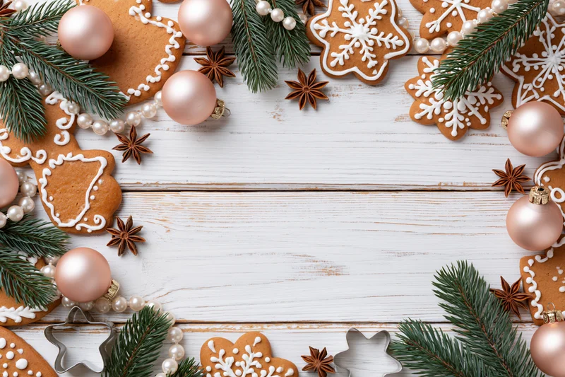 Gingerbread cookies and christmas ornaments arranged in a frame on a white wooden tabletop with copyspace in the center
