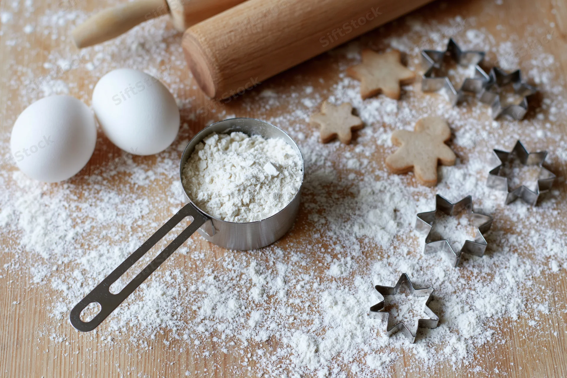 Flour and baking ingredients arranged on a wooden board with cookie cutters and rolling pin