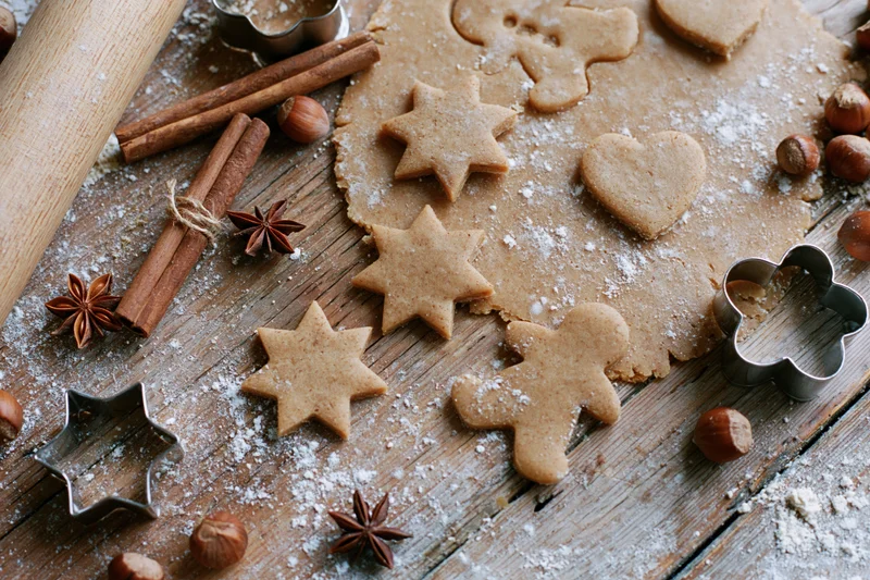 Gingerbread cookies cut into star, heart and gingerbreadman shapes on a floured wooden table with cinnamon sticks, hazelnuts and metal cutters