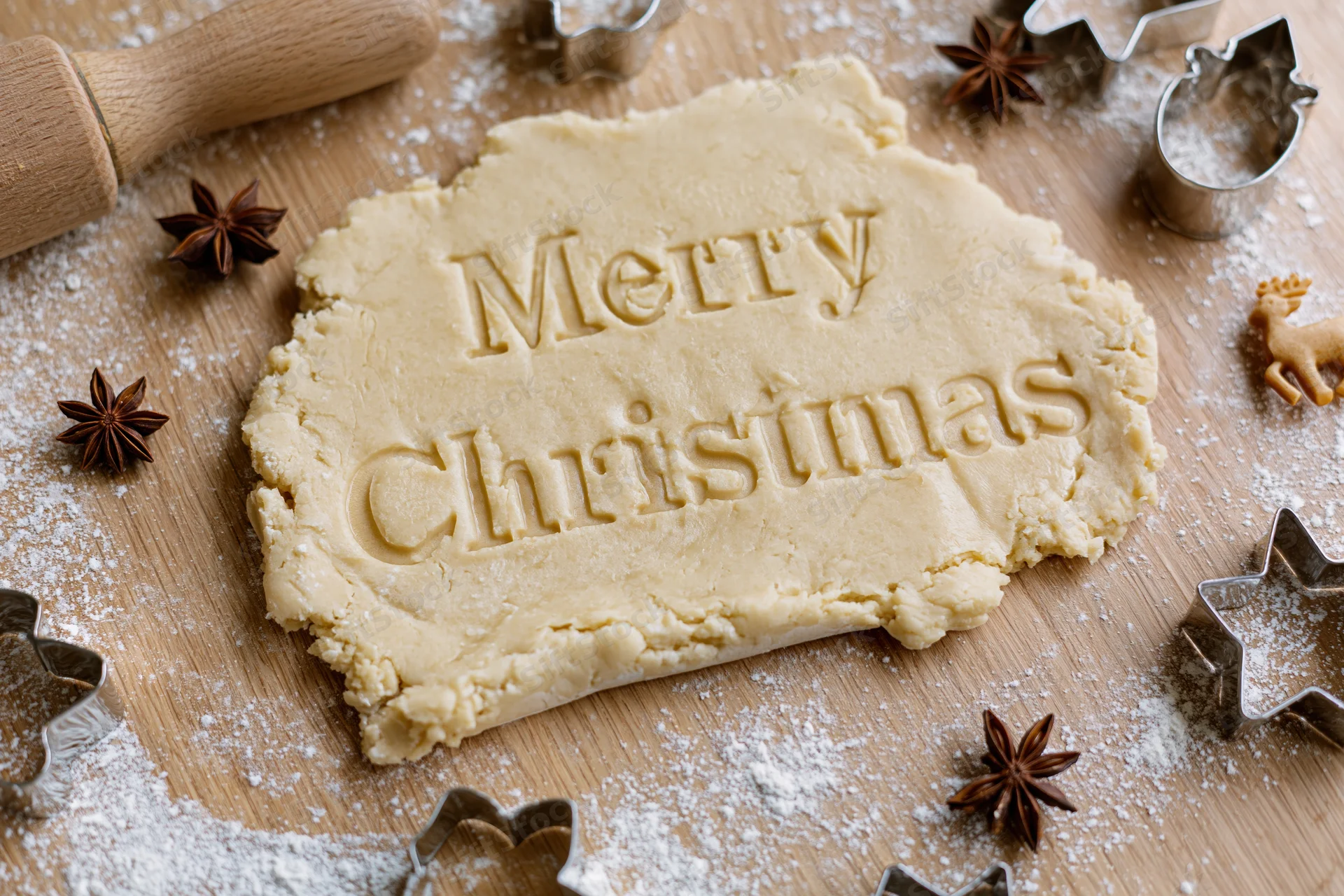 Christmas cookie dough with merry christmas text on wooden table surrounded by cutters and star anise