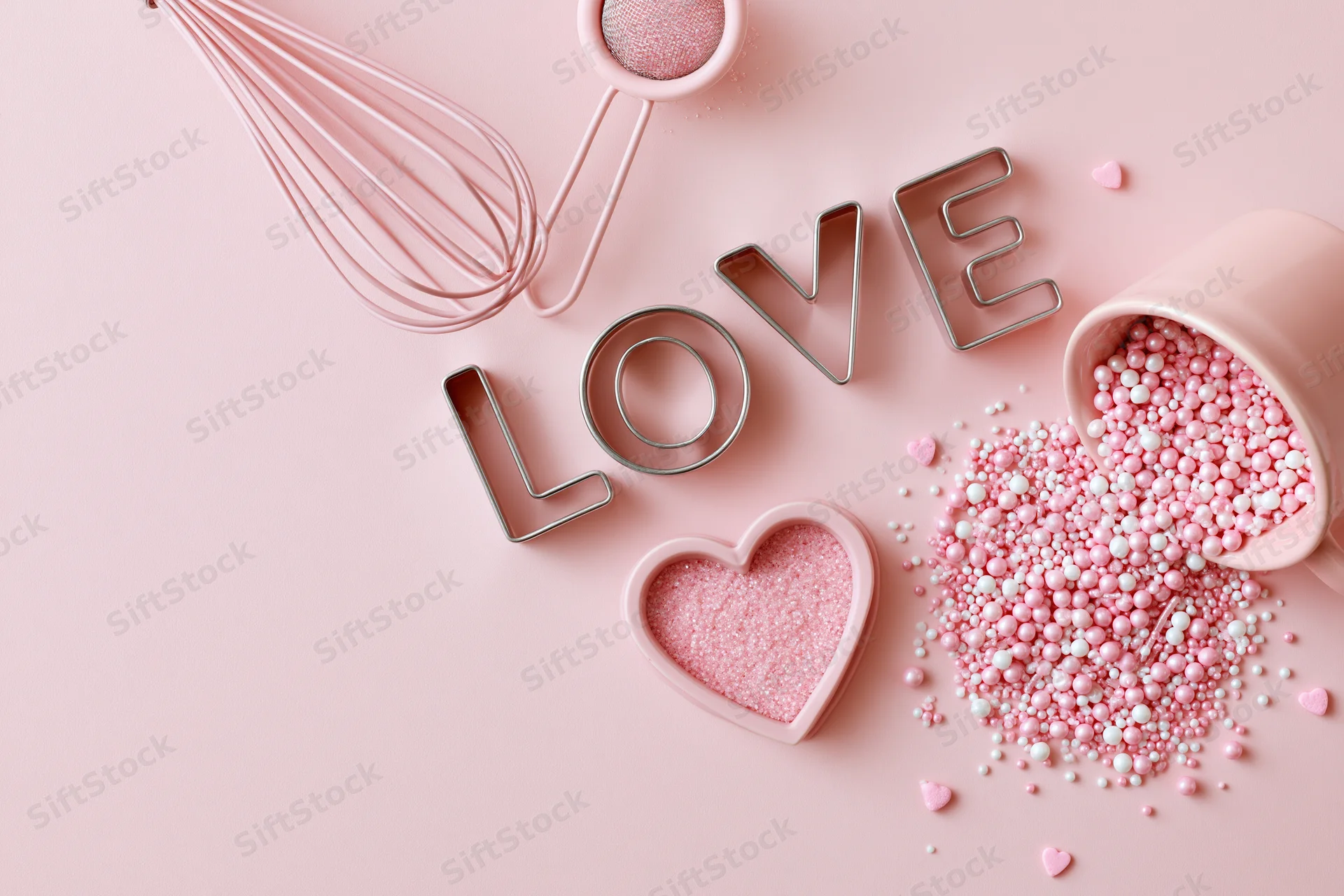 Pink baking tools and sprinkles arranged with love cookie cutters on a pastel surface