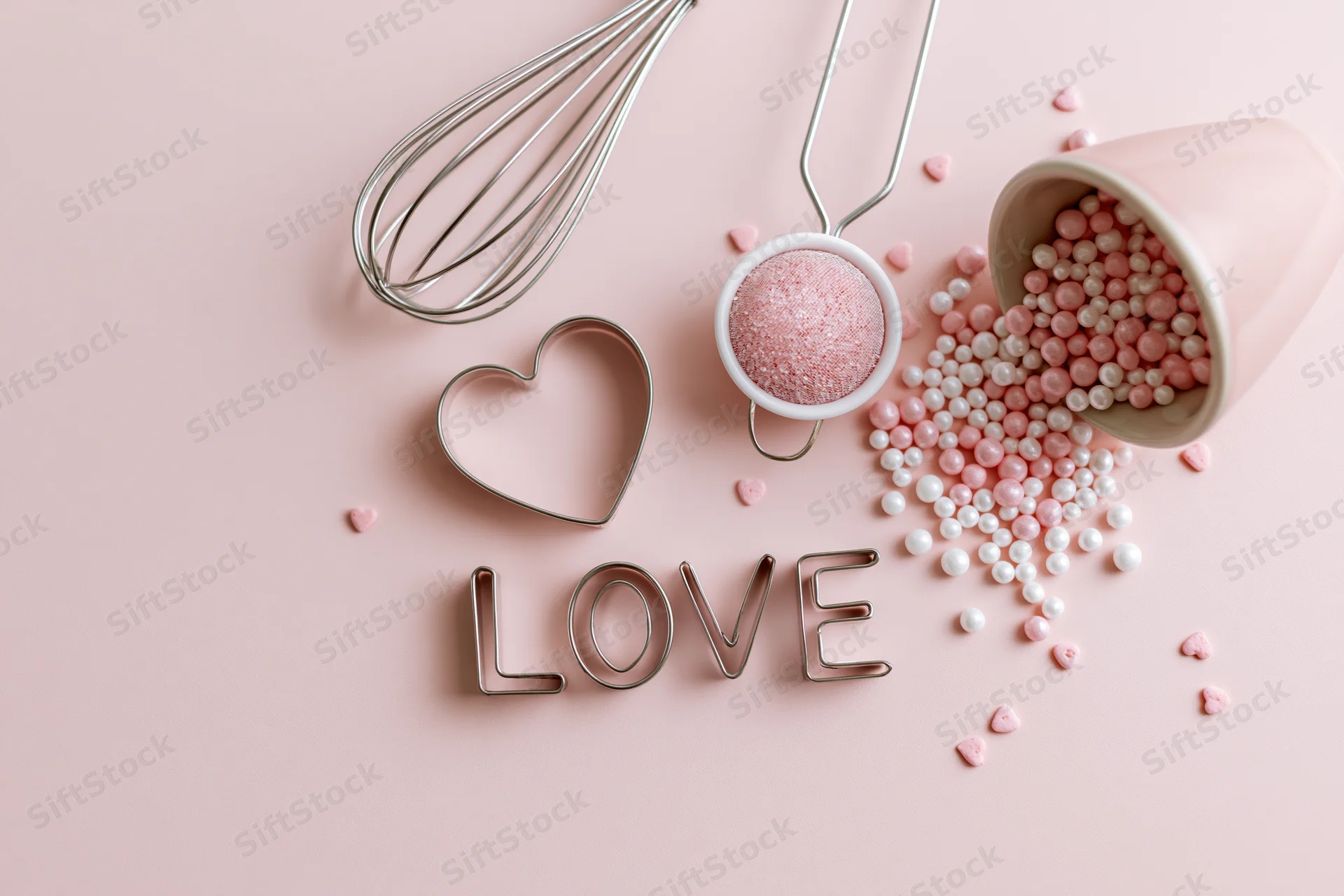 Baking tools and candy sprinkles arranged on pink surface with love cookie cutter and heart shapes