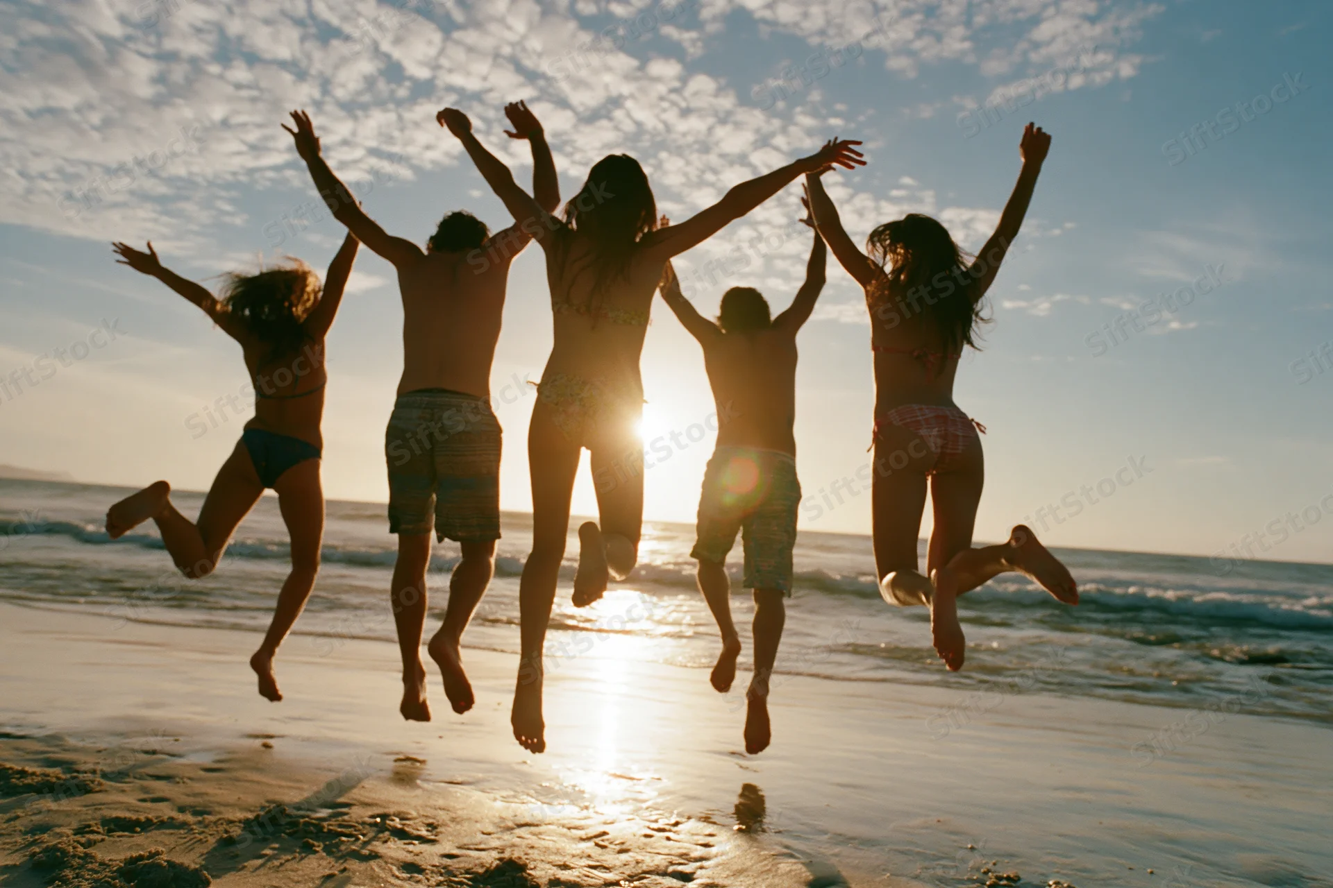 Five friends jumping together on a beach at sunset