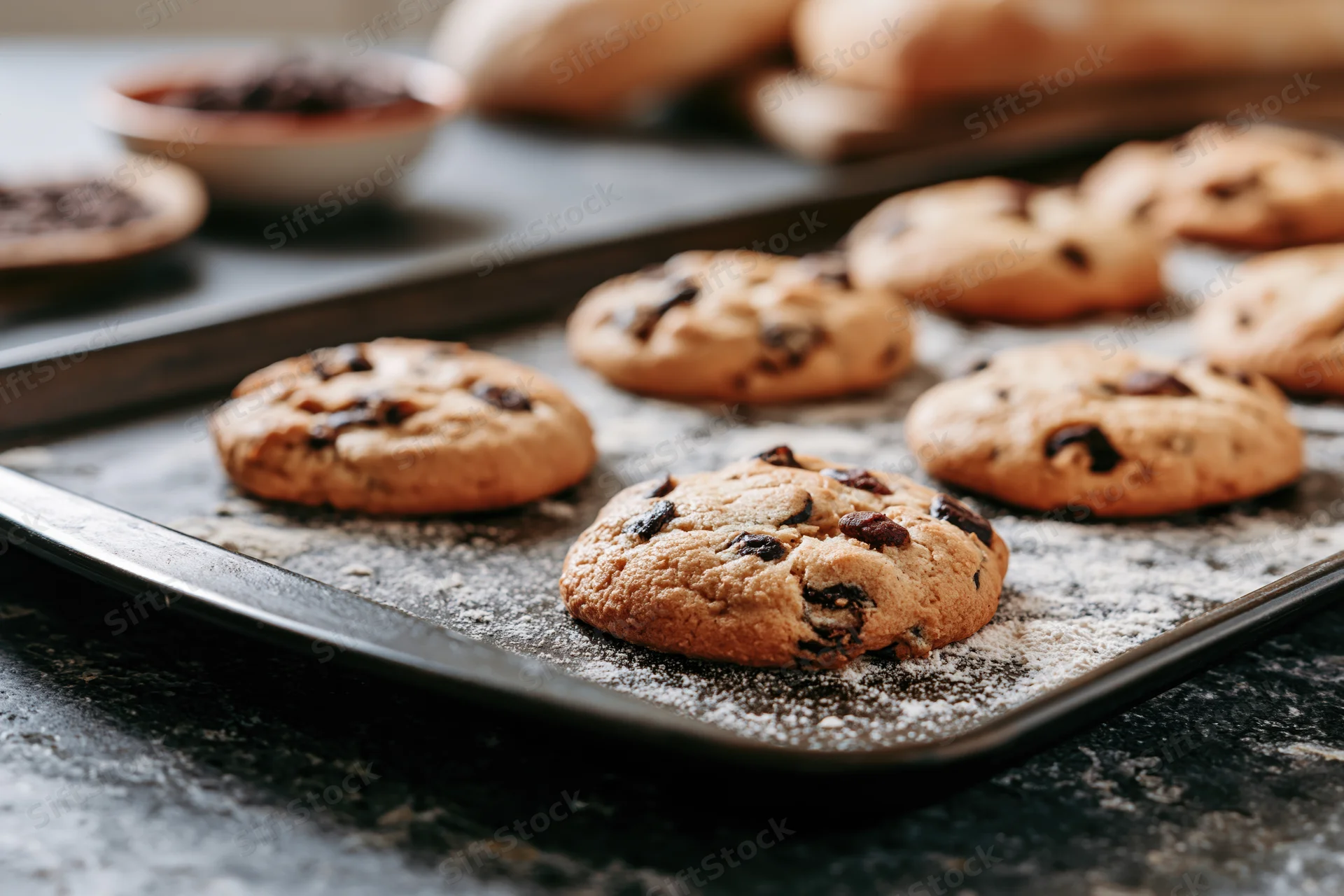Chocolate chip cookies on a baking tray dusted with flour on a dark countertop