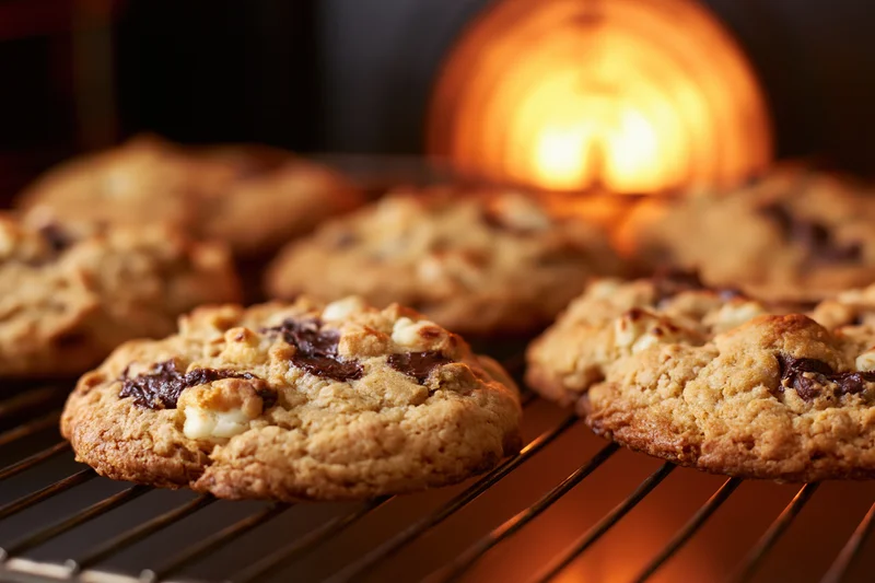 Freshly baked chocolate chip cookies cooling on a wire rack with warm oven light glowing in the background
