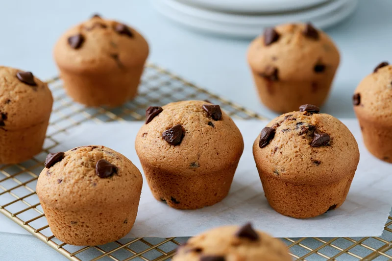 Chocolate chip muffins cooling on a wire rack with parchment paper in a kitchen setting