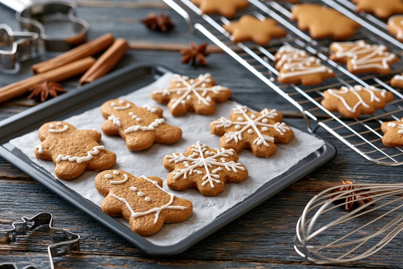 Gingerbread cookies decorated with white icing on a baking tray and cooling rack on a dark wooden countertop