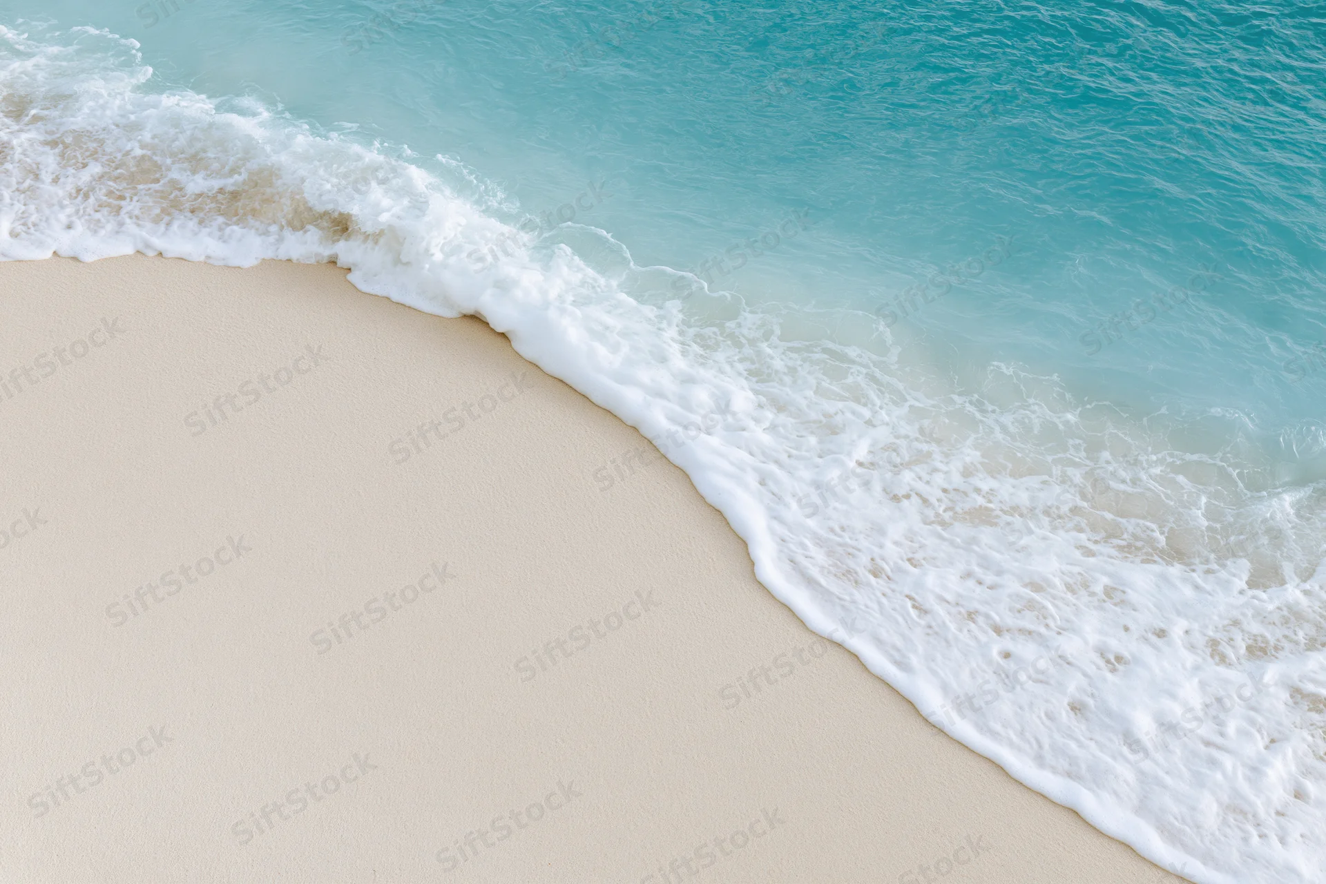 Gentle wave breaking on sandy beach with white foam and turquoise water