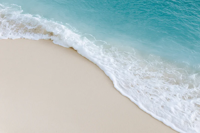 Gentle wave breaking on sandy beach with white foam and turquoise water