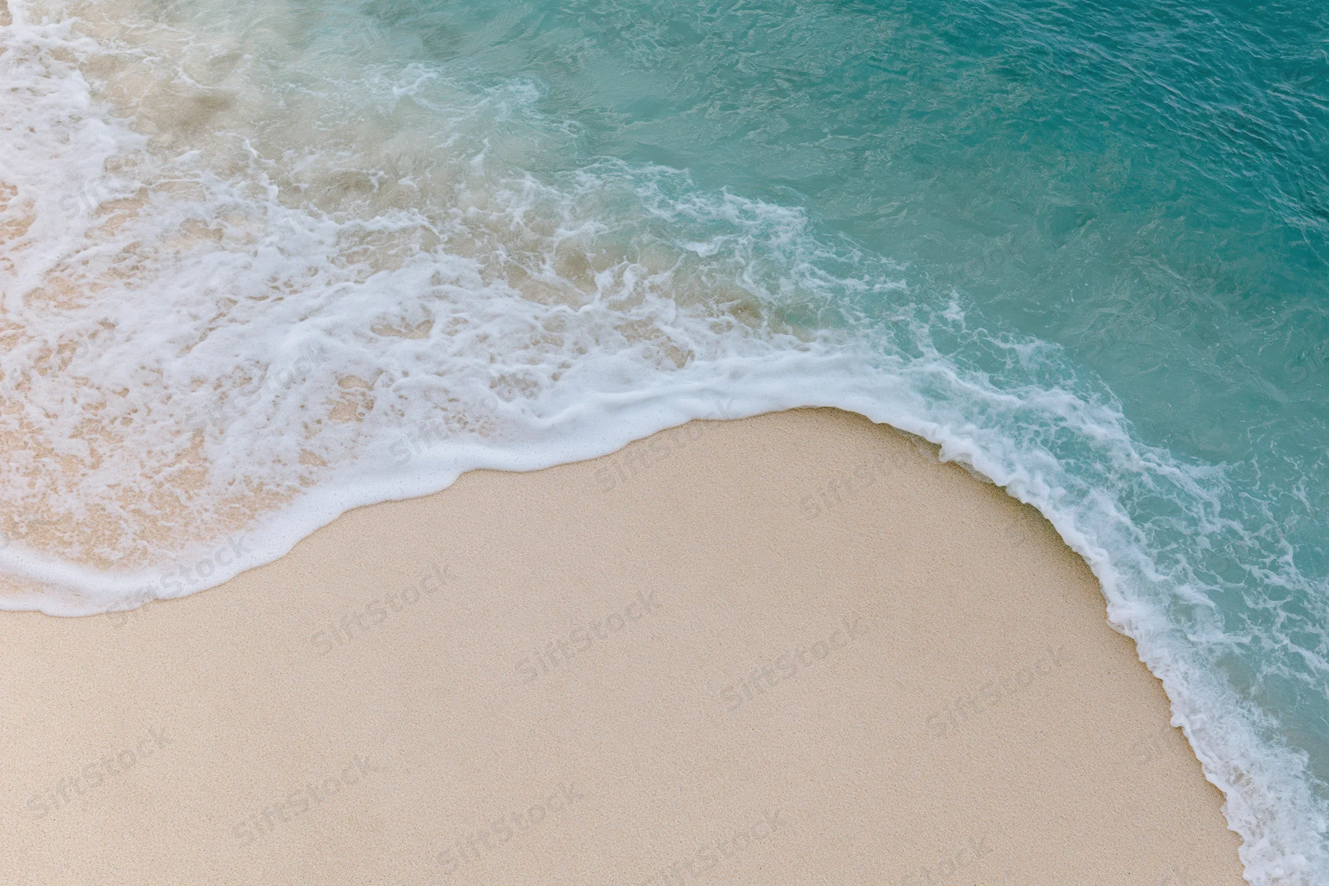 Gentle wave washing over sandy beach from above