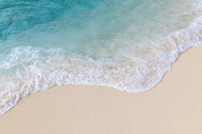 Gentle waves rolling onto a sandy beach with white foam and turquoise water