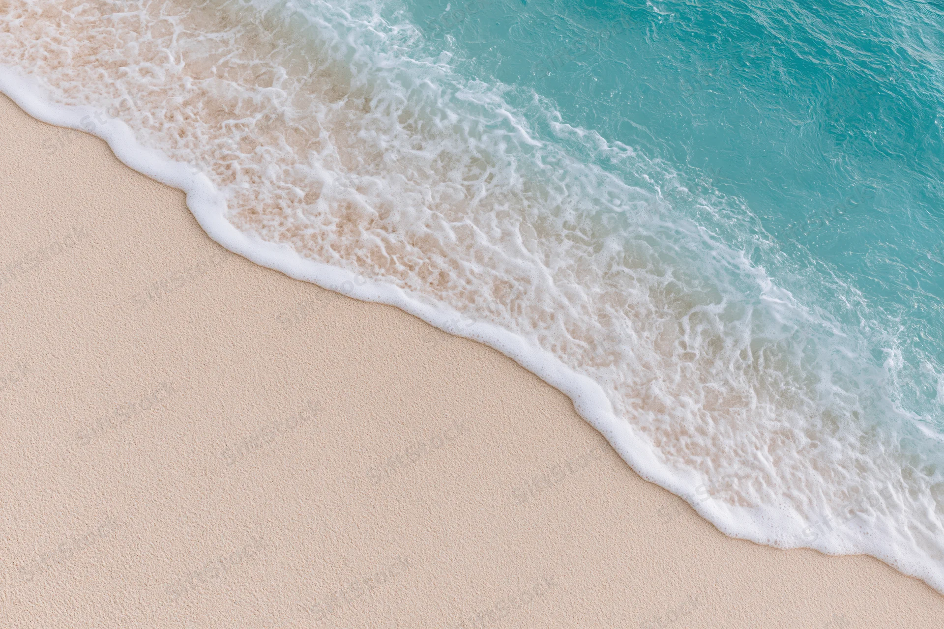 Turquoise ocean wave with white foam washing over light beige sand at the shoreline