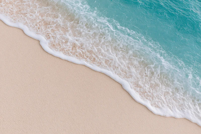 Turquoise ocean wave with white foam washing over light beige sand at the shoreline