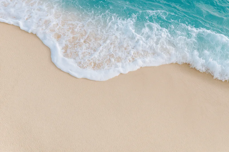 Gentle wave with white foam washing over smooth beige sand at the shoreline