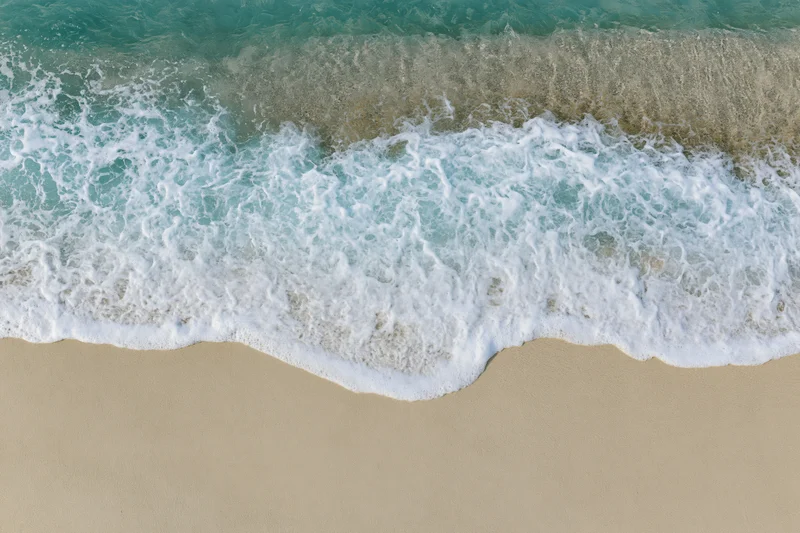 Waves breaking on sandy beach from overhead view
