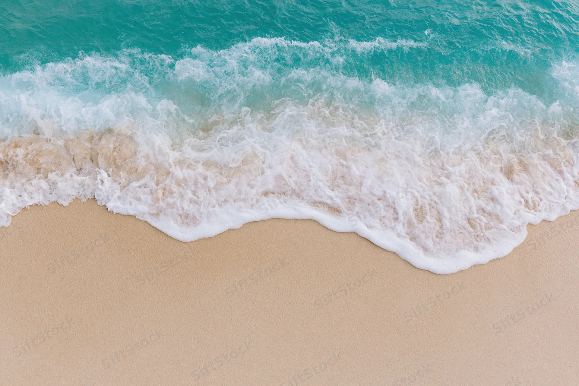 Turquoise ocean wave breaking onto sandy beach from above