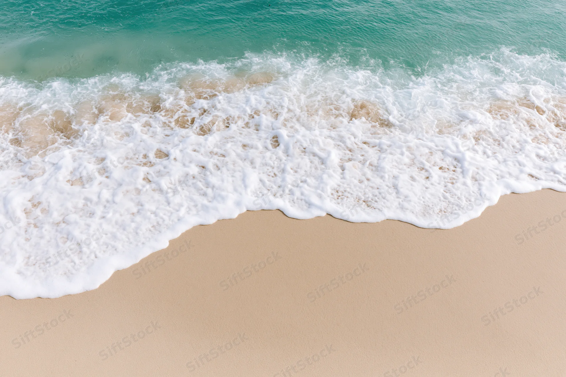 Gentle ocean wave with white foam washing onto sandy beach