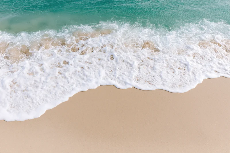 Gentle ocean wave with white foam washing onto sandy beach